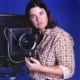 Photo of a brown haired light skinned person next to a 16x20" camera